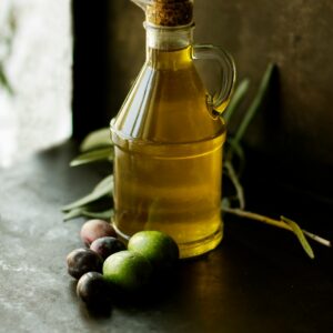 Glass cruet of golden olive oil with fresh olives